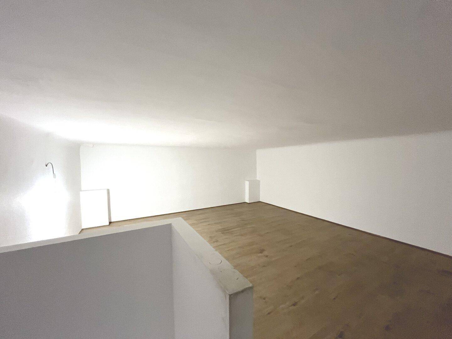 Obergeschoss eines Geschäftsraums mit Holzboden und weißen Wänden, von der Treppe aus gesehen.