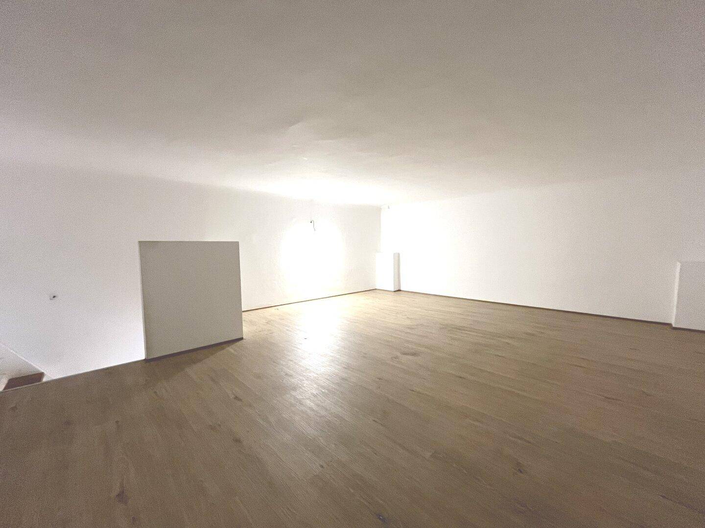 Geräumiger, heller Raum im Obergeschoss mit Holzboden und weiß gestrichenen Wänden.