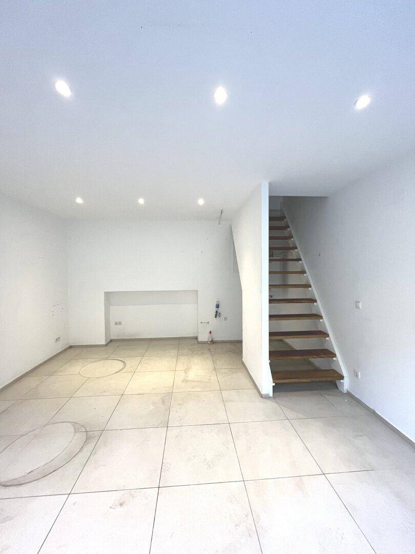 Heller Geschäftsraum mit Fliesenboden und einer Holztreppe, die in eine obere Etage führt.
