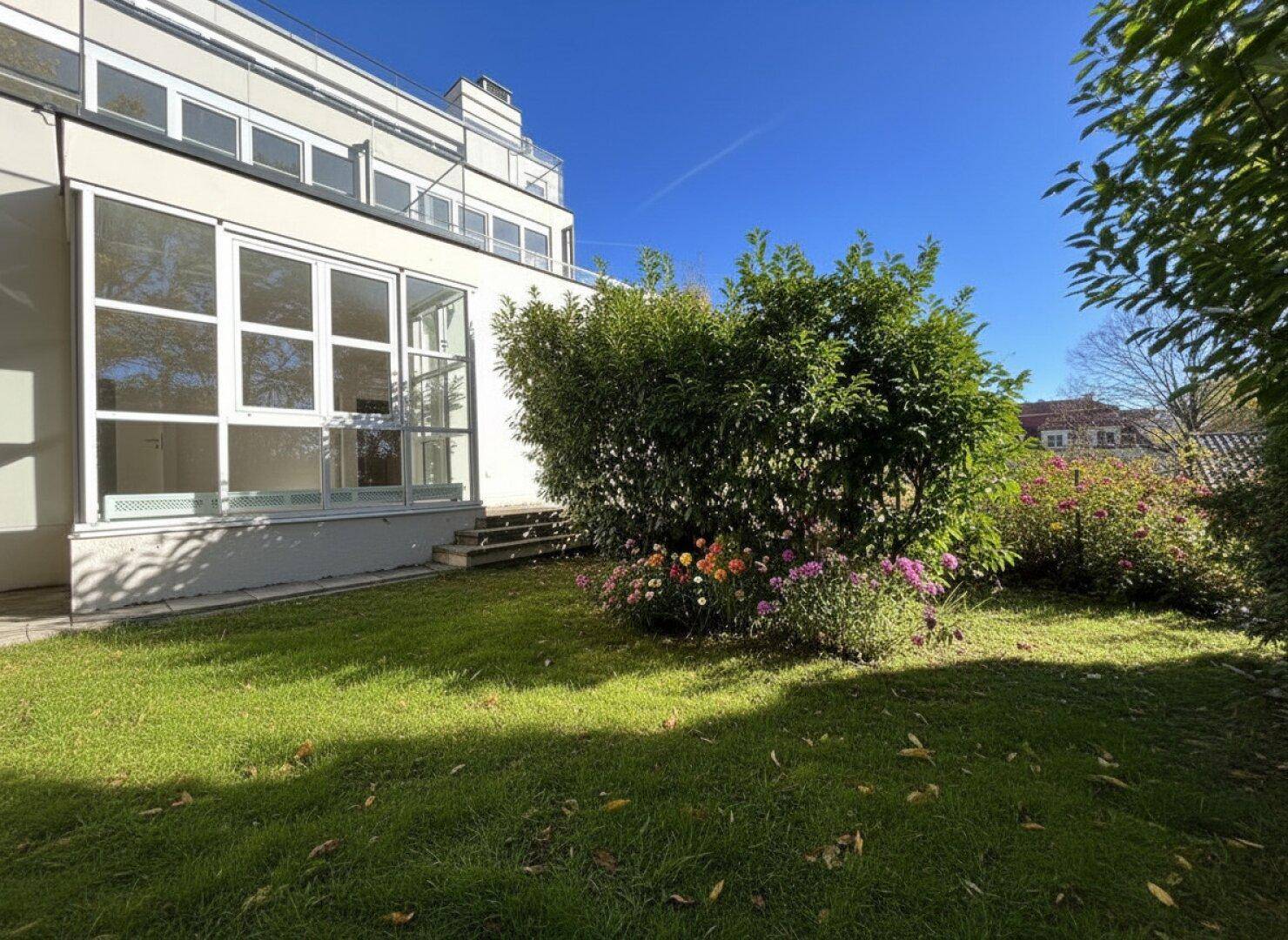 Gepflegter Gartenbereich mit Rasen und Blumenbeeten neben dem modernen Gebäude.