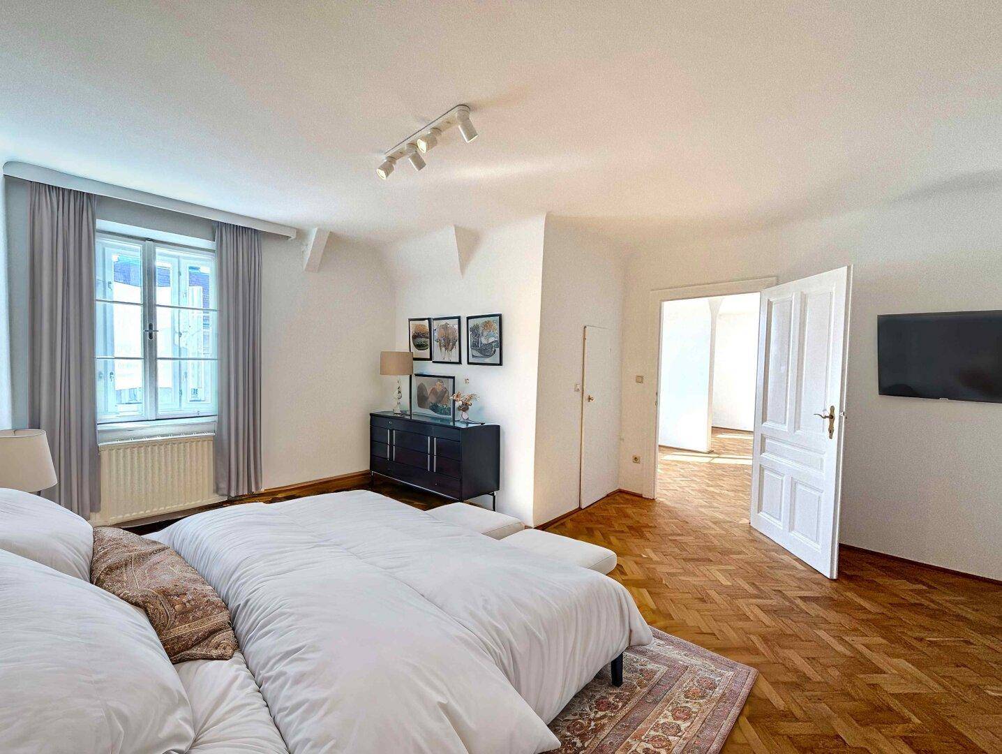 Geräumiges Schlafzimmer mit Parkettboden, großem Bett und Zugang zu weiteren Räumen.
