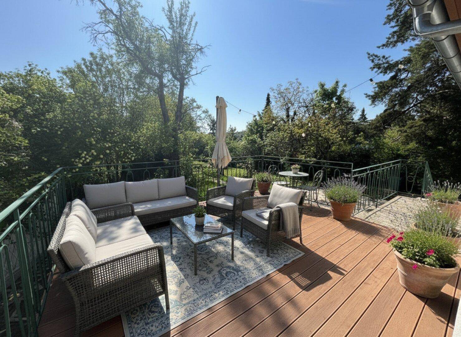 Geräumige Holzterrasse mit modernen Lounge-Möbeln, Pflanzen und weitem Blick ins Grüne.