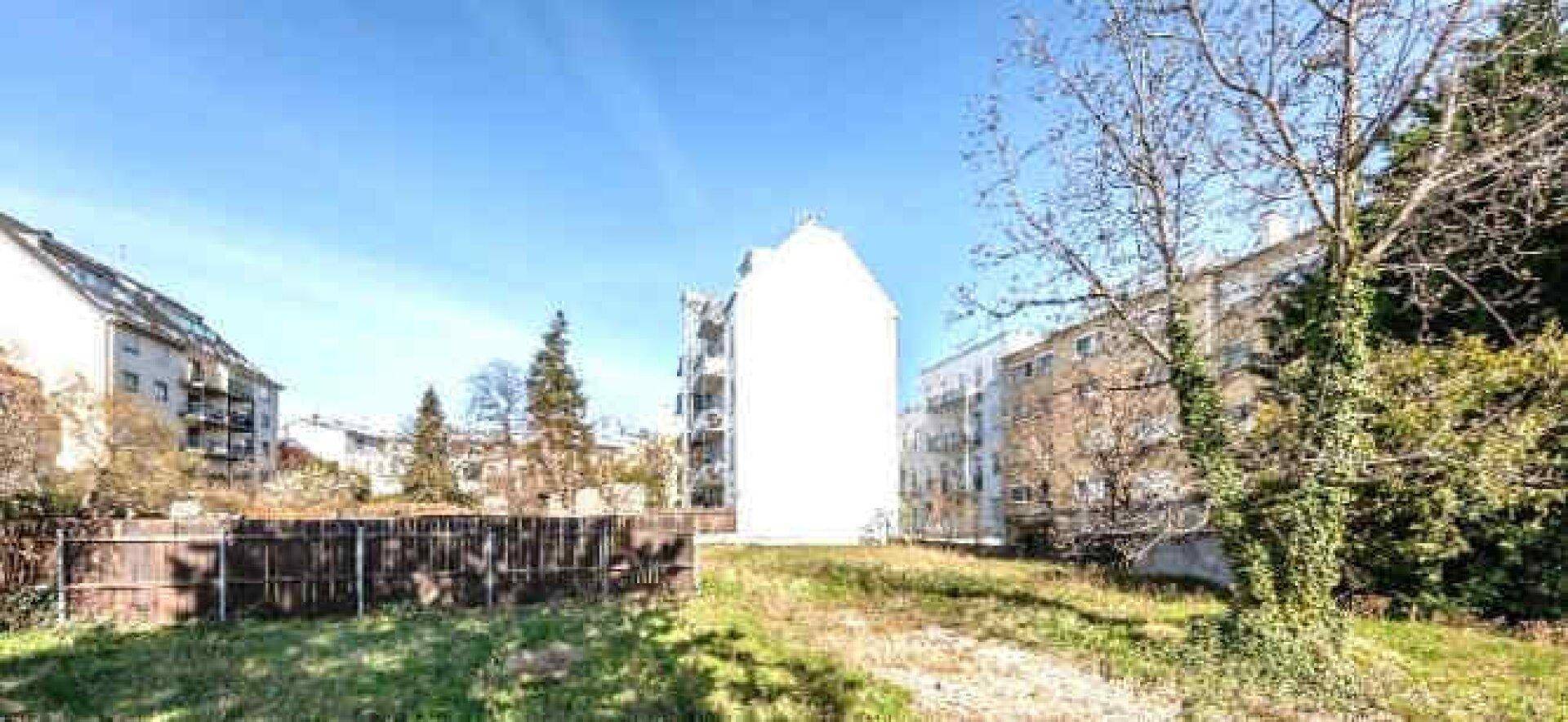Panoramablick auf eine unbebaute Grünfläche mit umliegenden Wohngebäuden und Bäumen.