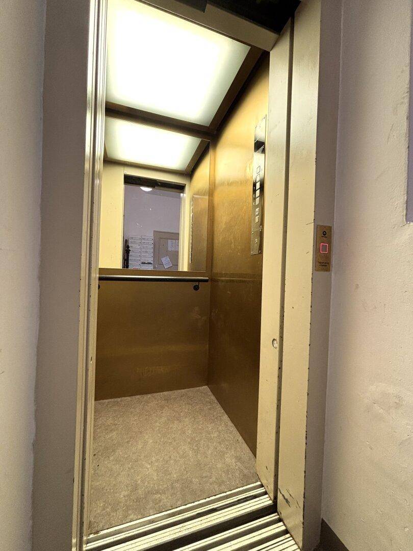 Alter Aufzug mit goldfarbenen Wänden und Spuren von Abnutzung im Gebäude.