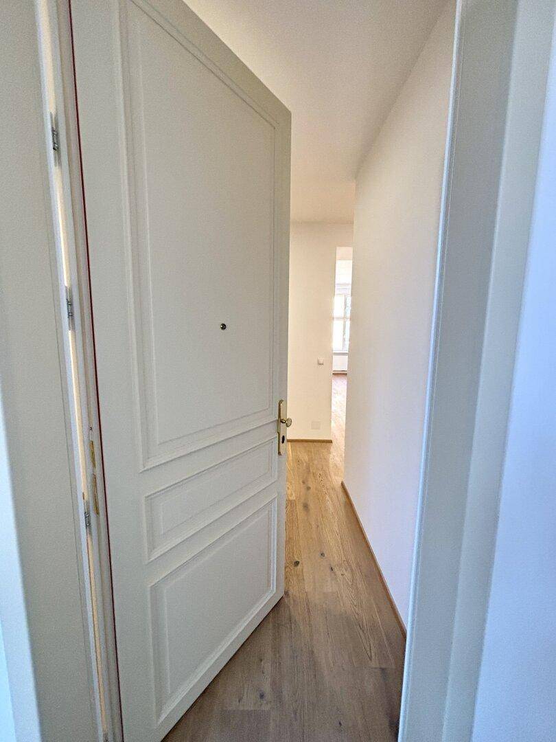 Offene weiße Kassettentür, die den Blick in einen hellen Flur mit Holzboden freigibt.