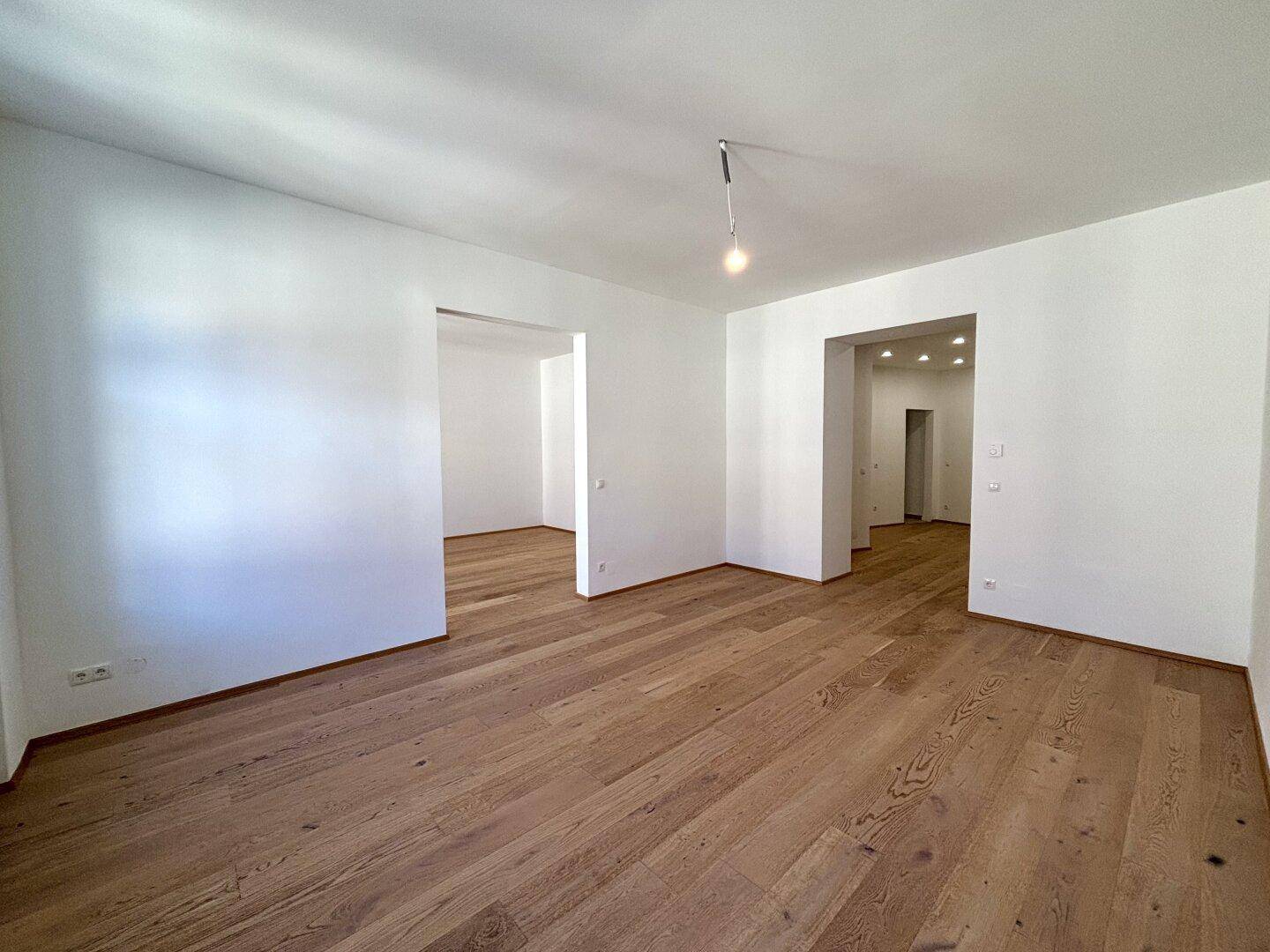 Großer, heller Raum mit Holzboden und mehreren offenen Durchgängen zu anderen Bereichen.