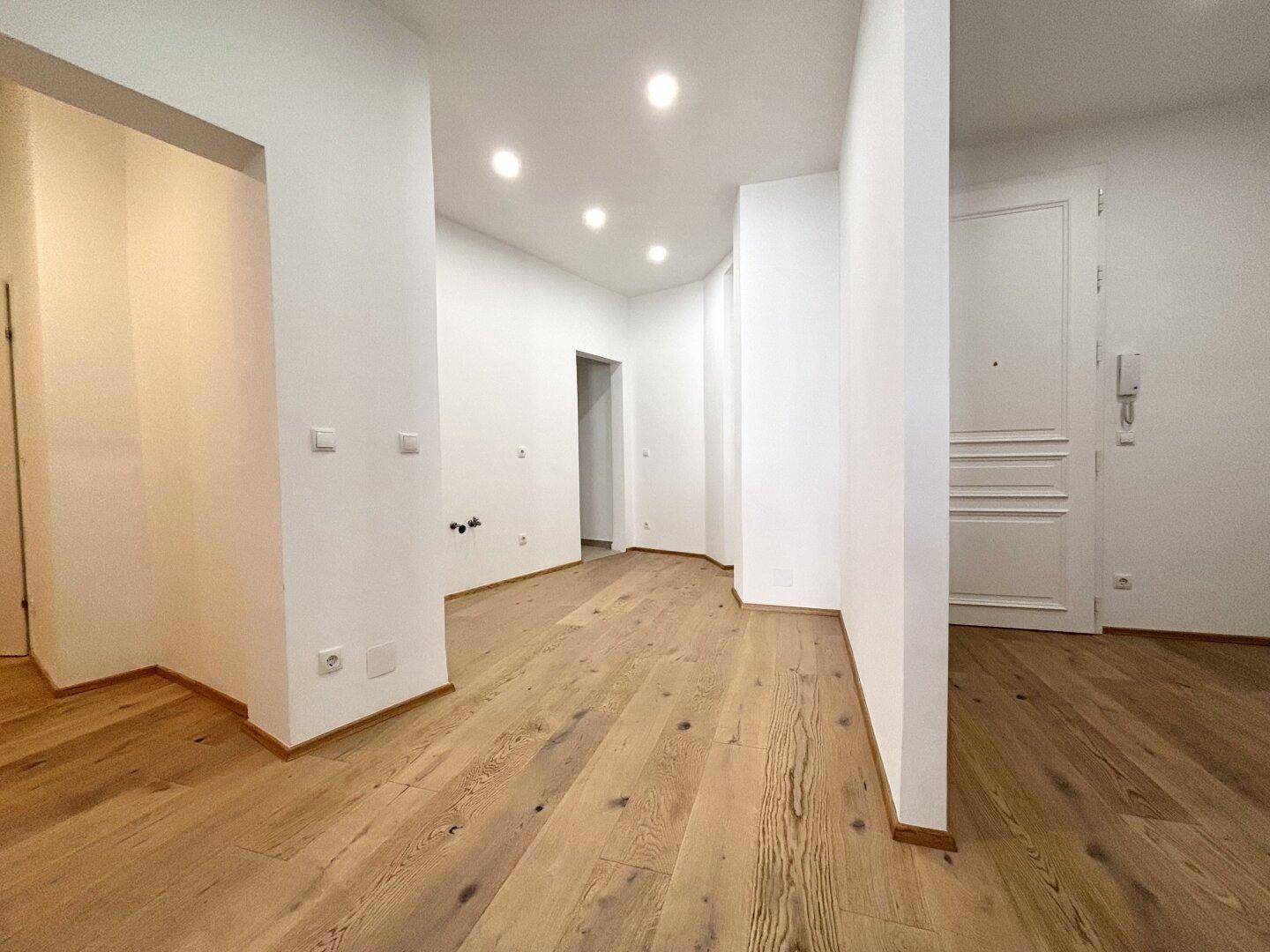 Heller Flur mit Holzboden und Einbaustrahlern, der zu verschiedenen Zimmern führt.