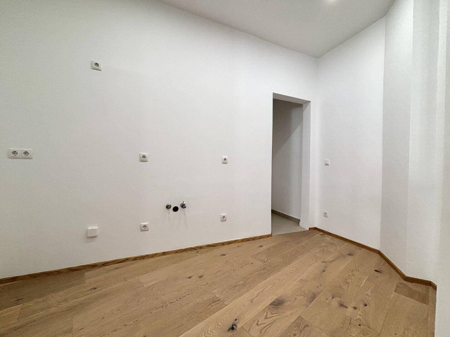 Kleiner, heller Raum mit Holzboden und Anschlüssen, ideal als Hauswirtschaftsraum nutzbar.