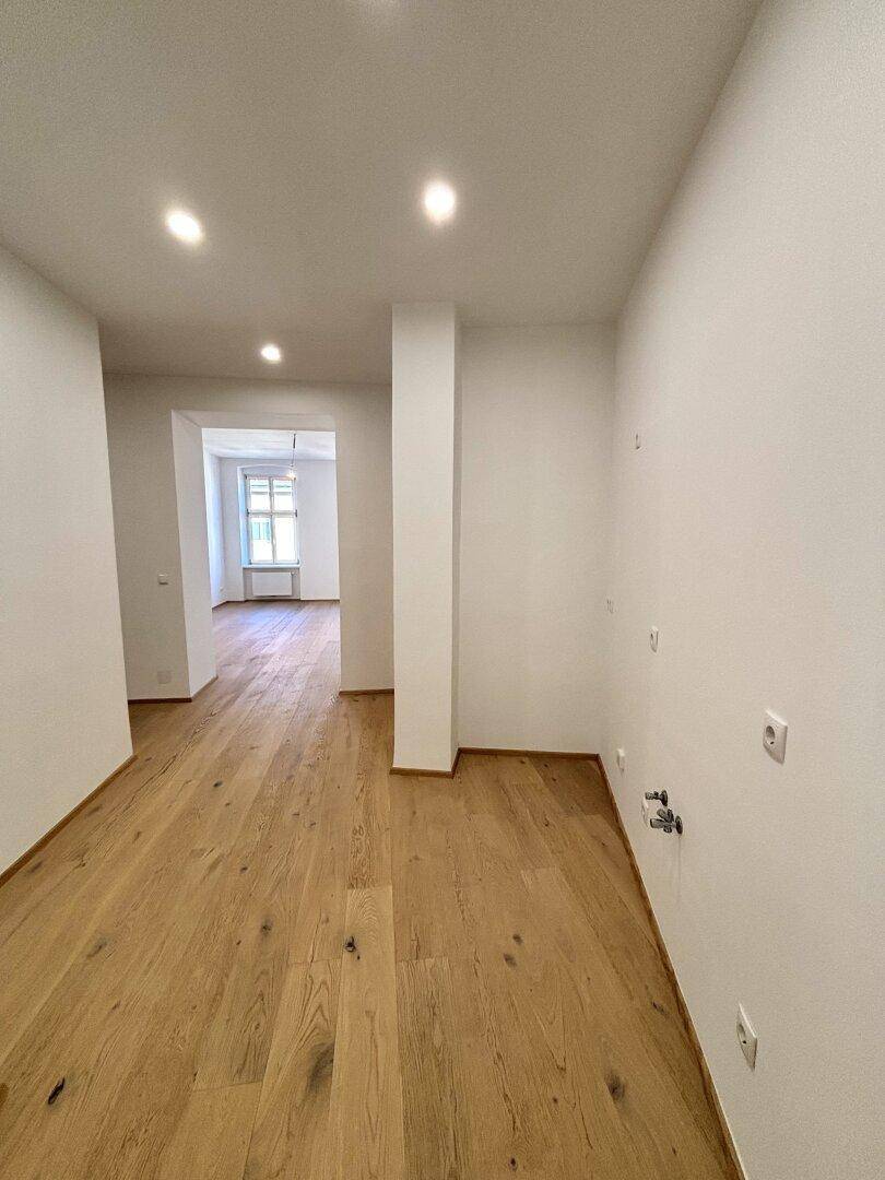 Leerer Raum mit Holzboden und Anschlüssen für eine Küche, bereit für den Einbau.