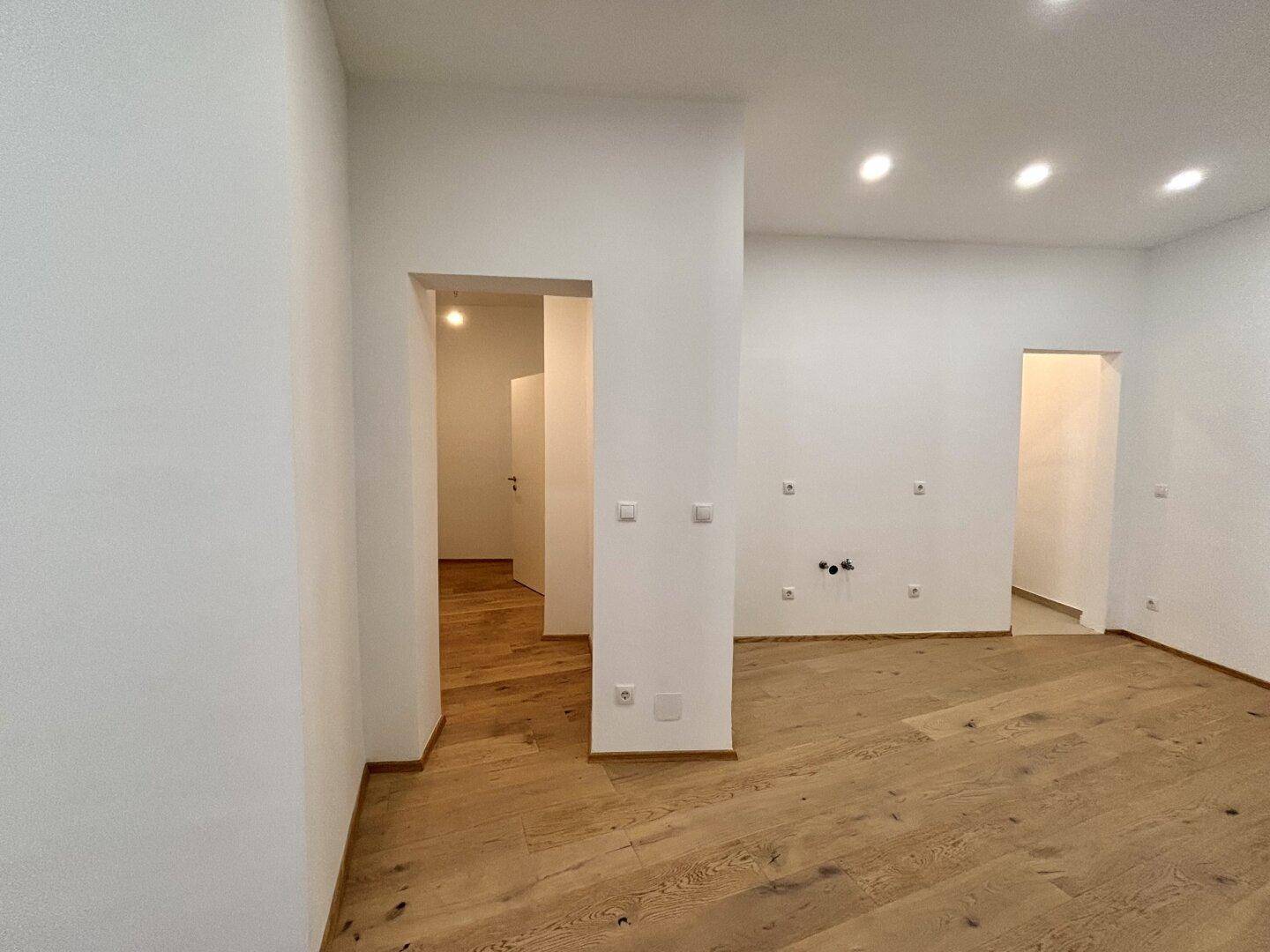 Heller Flur mit Holzboden und Einbaustrahlern, der zu verschiedenen Zimmern führt.
