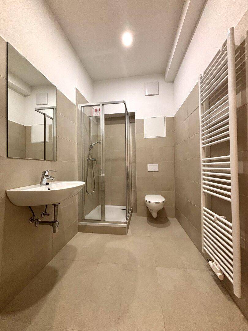 Modernes Badezimmer mit Duschkabine, Waschbecken, WC und beheiztem Handtuchhalter.