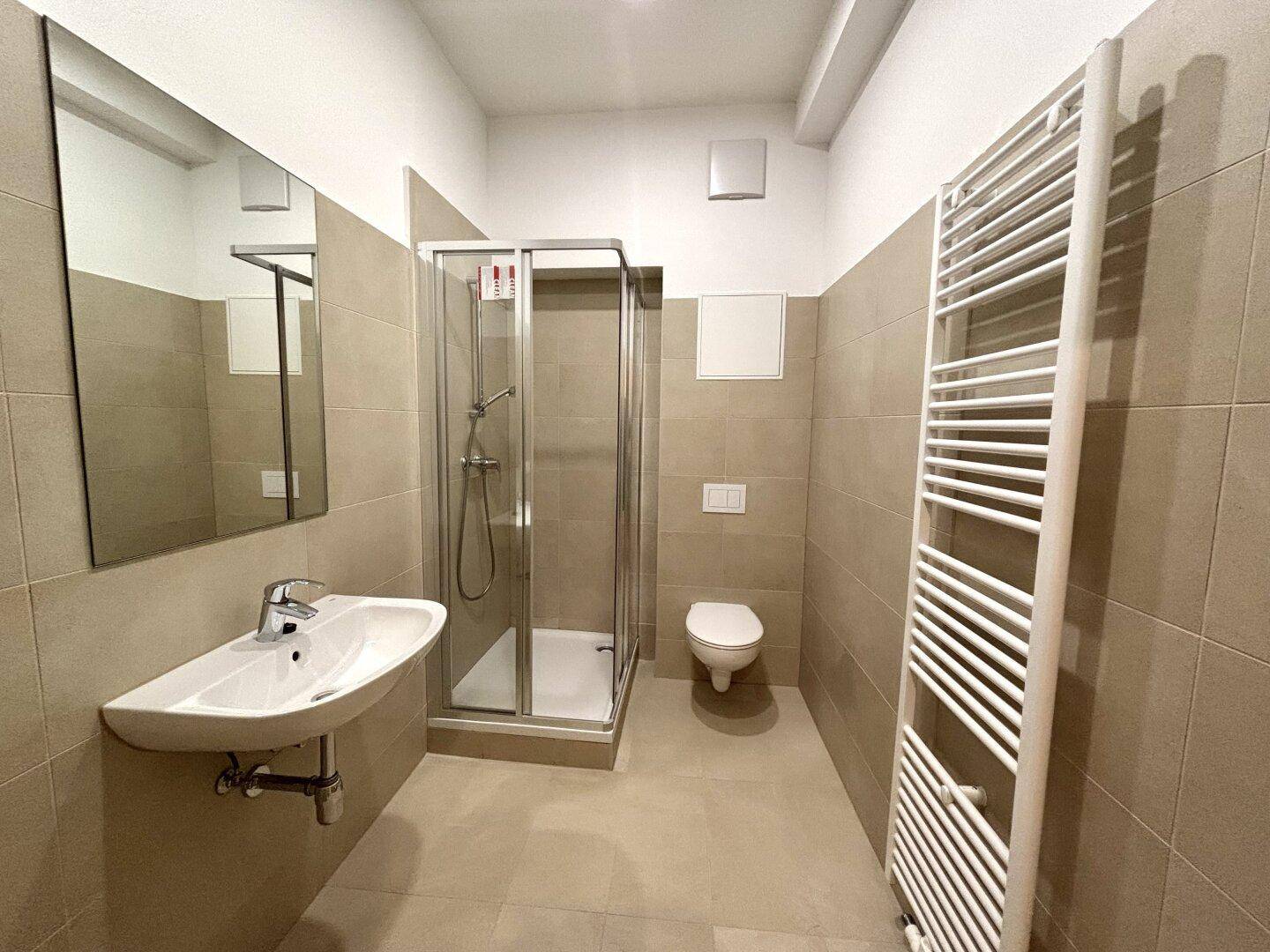Modernes Badezimmer mit Dusche, WC, Waschbecken und beheiztem Handtuchhalter.