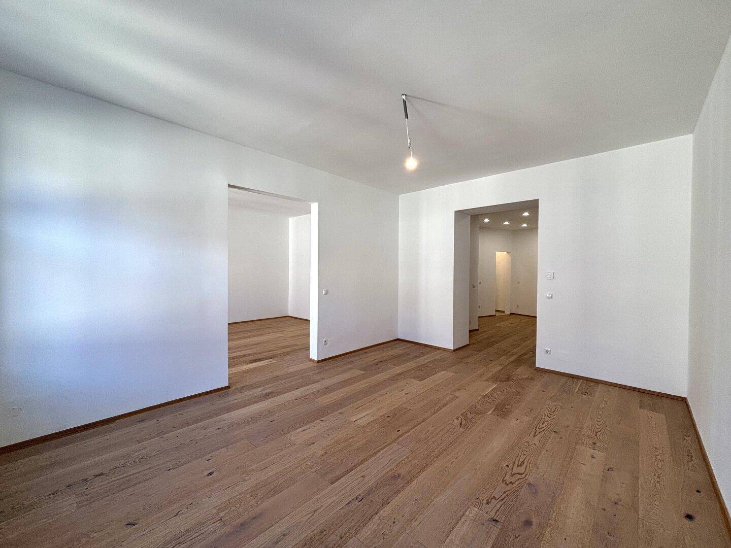 Großer, heller Raum mit Holzboden und mehreren offenen Durchgängen zu anderen Bereichen.