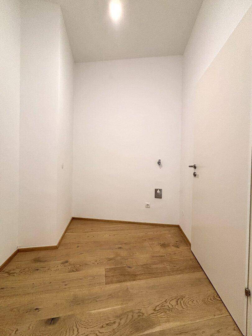 Kleiner, heller Raum mit Holzboden und Anschlüssen, ideal als Hauswirtschaftsraum nutzbar.