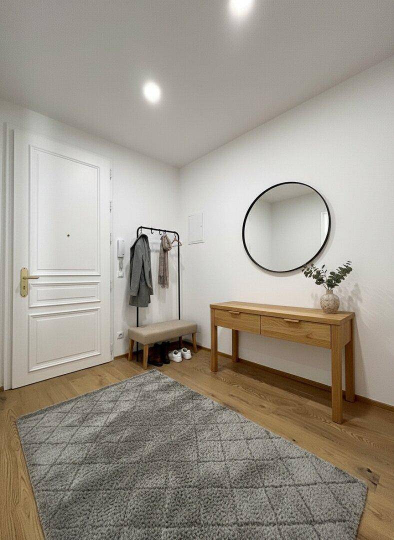 Heller Eingangsbereich mit Holzboden, Garderobe und einem runden Spiegel über einer Holzkonsole.