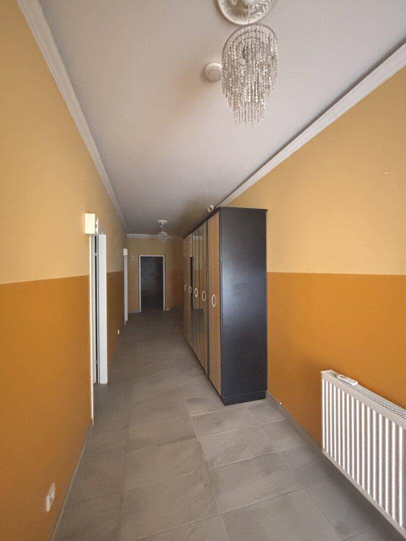 Langer, schmaler Flur mit zweifarbigen Wänden, Fliesenboden, einem großen Schrank und einem Kronleuchter.