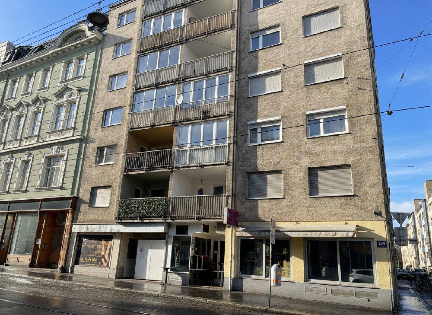 Nahaufnahme der Fassade eines Wohn- und Geschäftshauses mit mehreren Balkonen und Rollläden an den Fenstern.