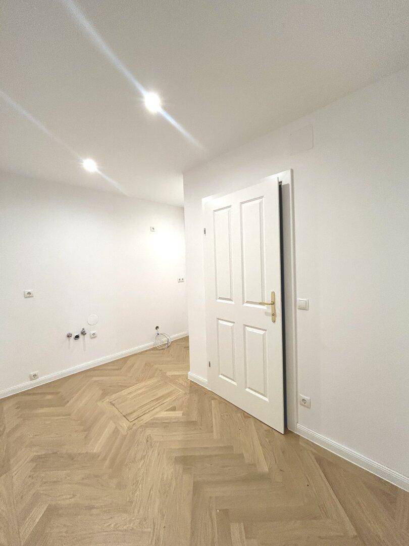 Kleiner Raum mit Fischgrätparkett und einer weißen Tür, vorbereitet für weitere Installationen.