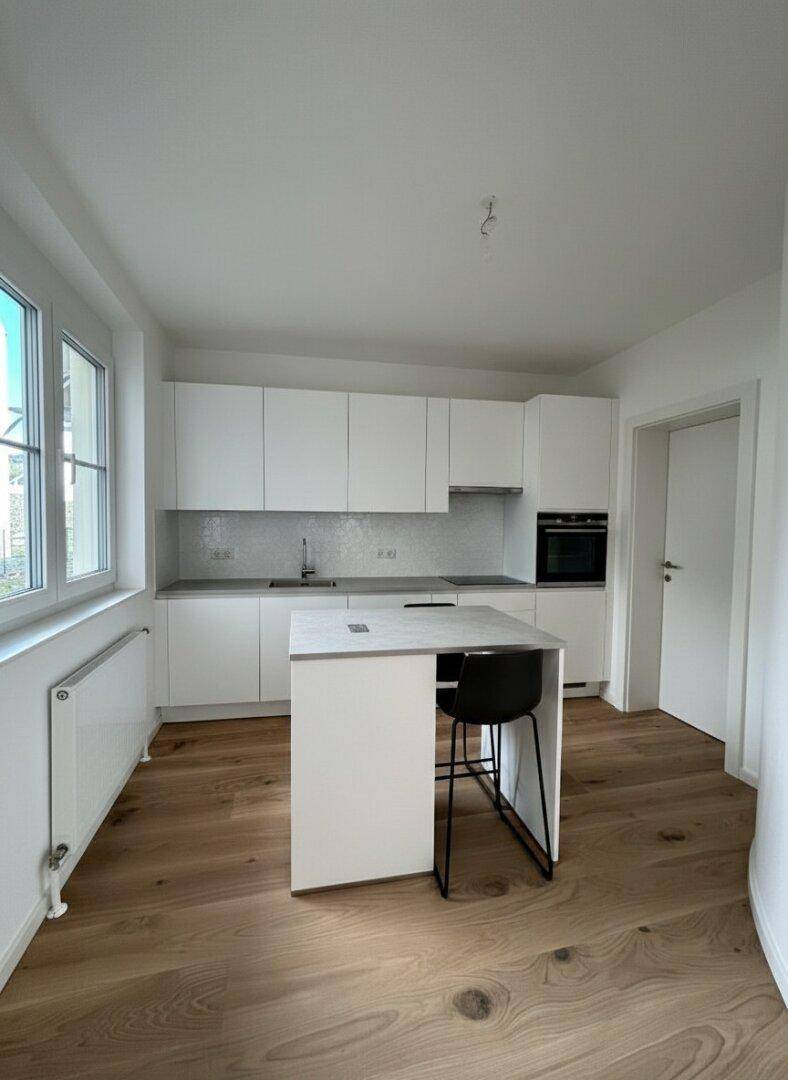Moderne weiße Küche mit Holzboden, Kücheninsel und integrierten Geräten.