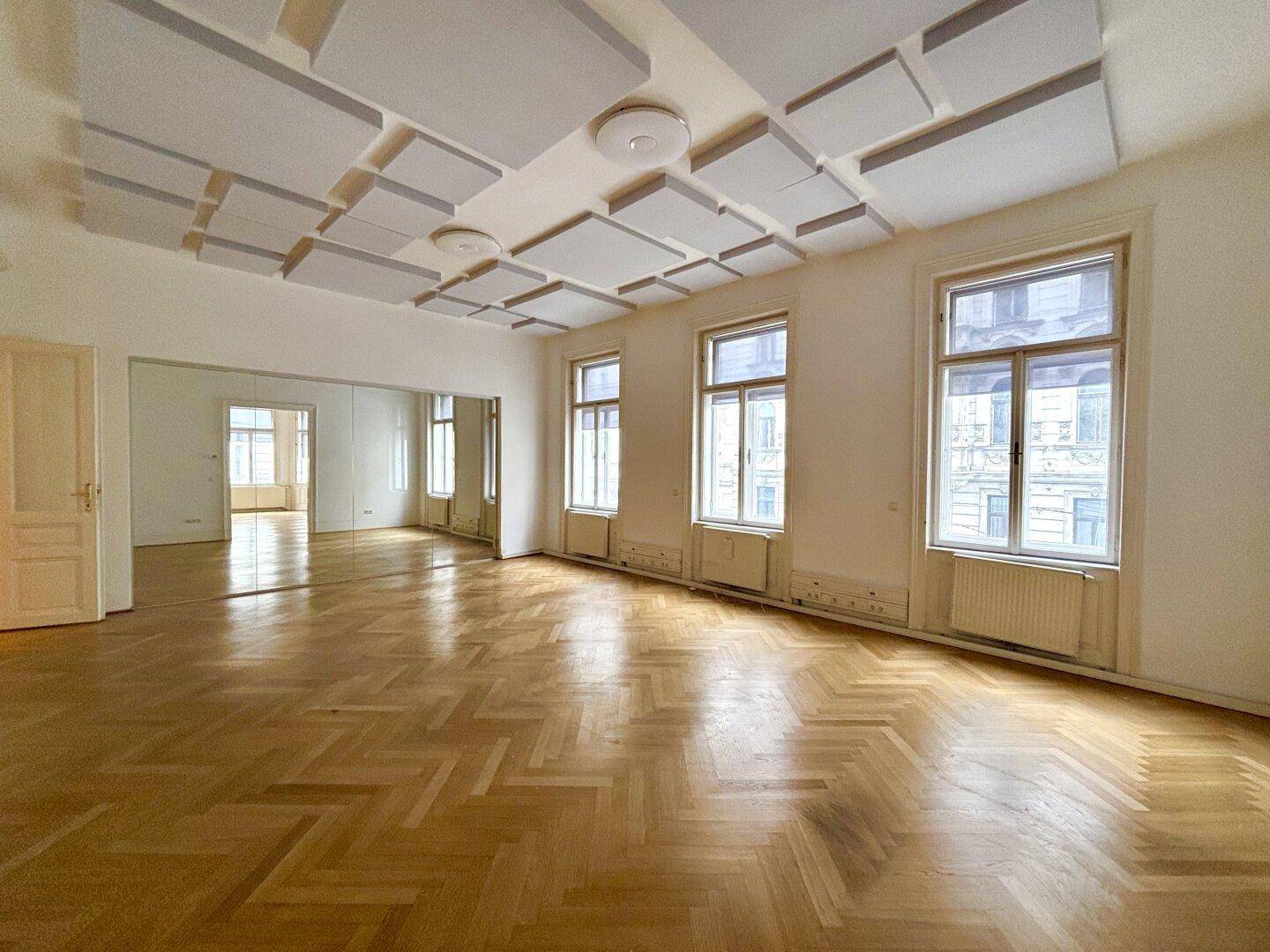 Heller Raum mit Fischgrätparkett, Schalldämmplatten an der Decke und Blick auf die Straße.