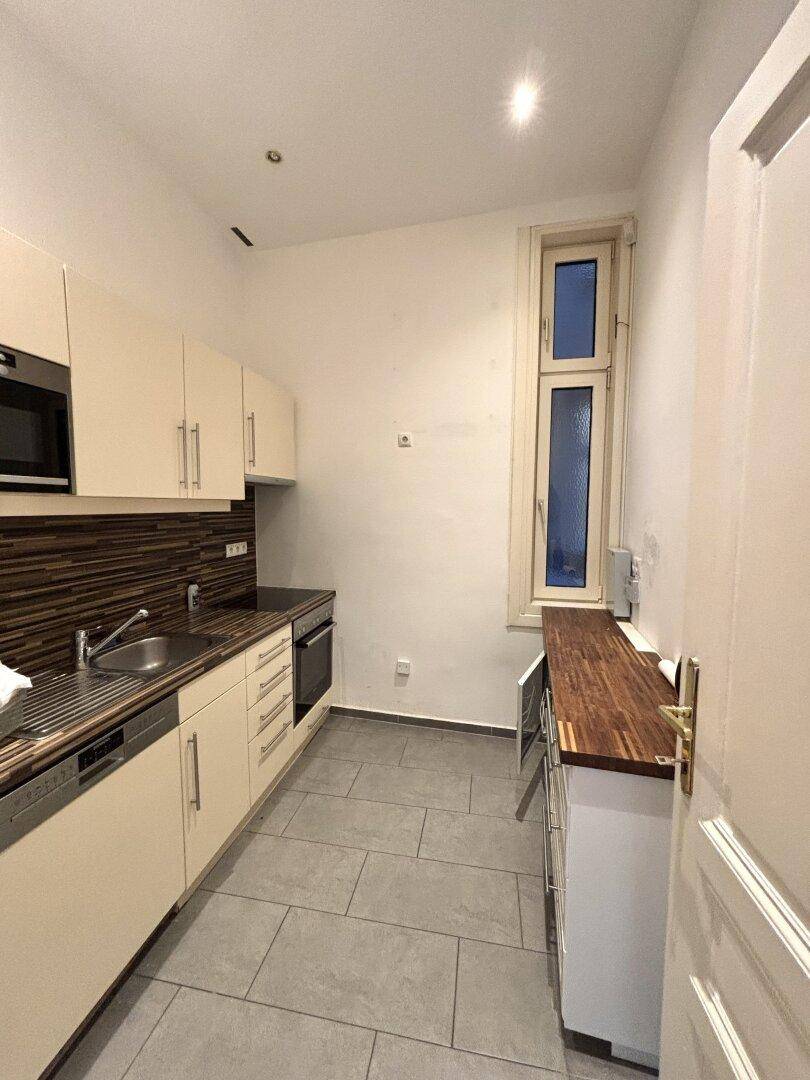 Schmale Küche mit beigen Schränken, Holz-Arbeitsplatte und Fliesenboden.