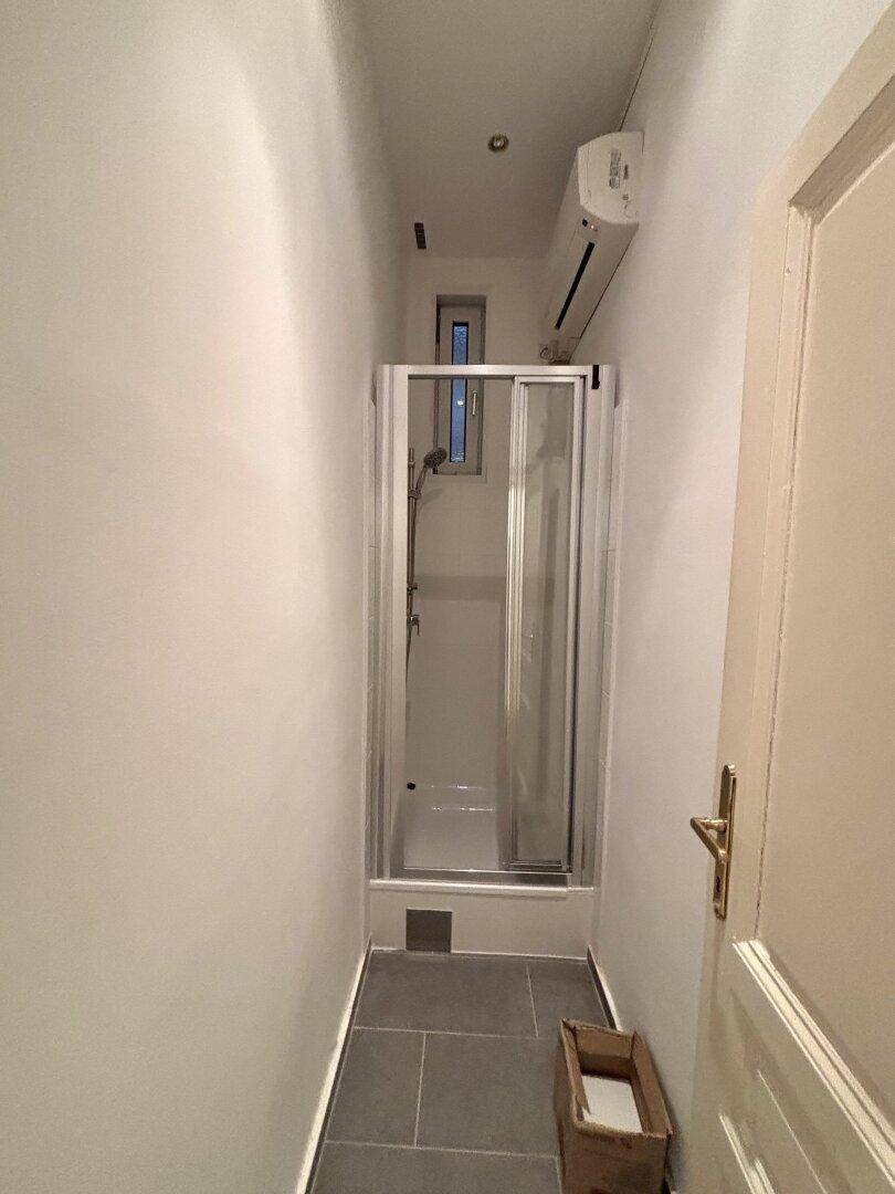 Kleines Badezimmer mit Duschkabine, Fliesenboden und schmalem Fenster.