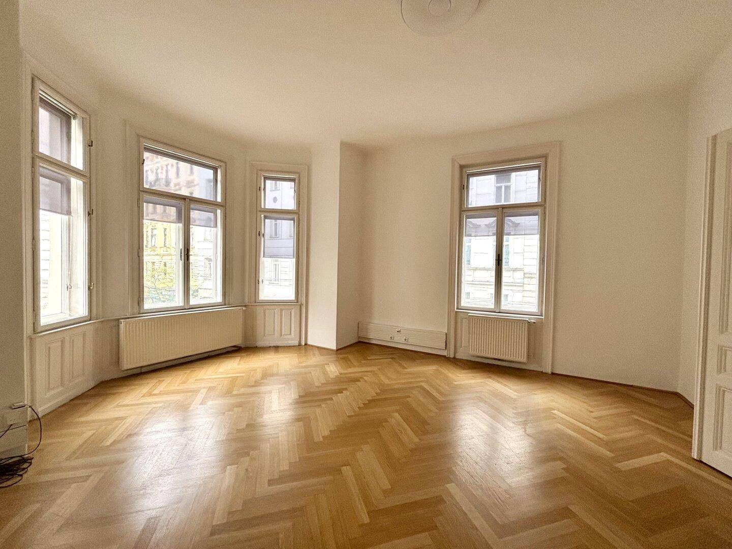 Heller Raum mit Fischgrätparkett, Erkerfenstern und Blick auf die Umgebung.