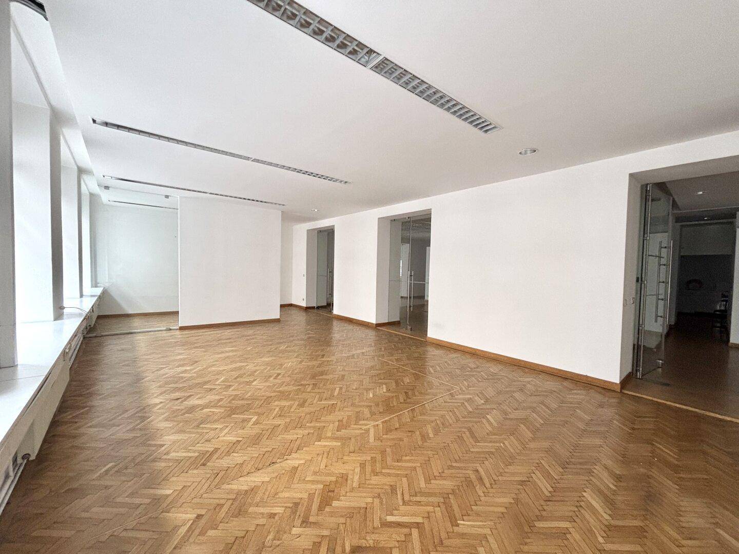 Geräumiger Hauptbürobereich mit Fischgrätparkett, weißen Wänden und viel natürlichem Licht durch die Fenster.