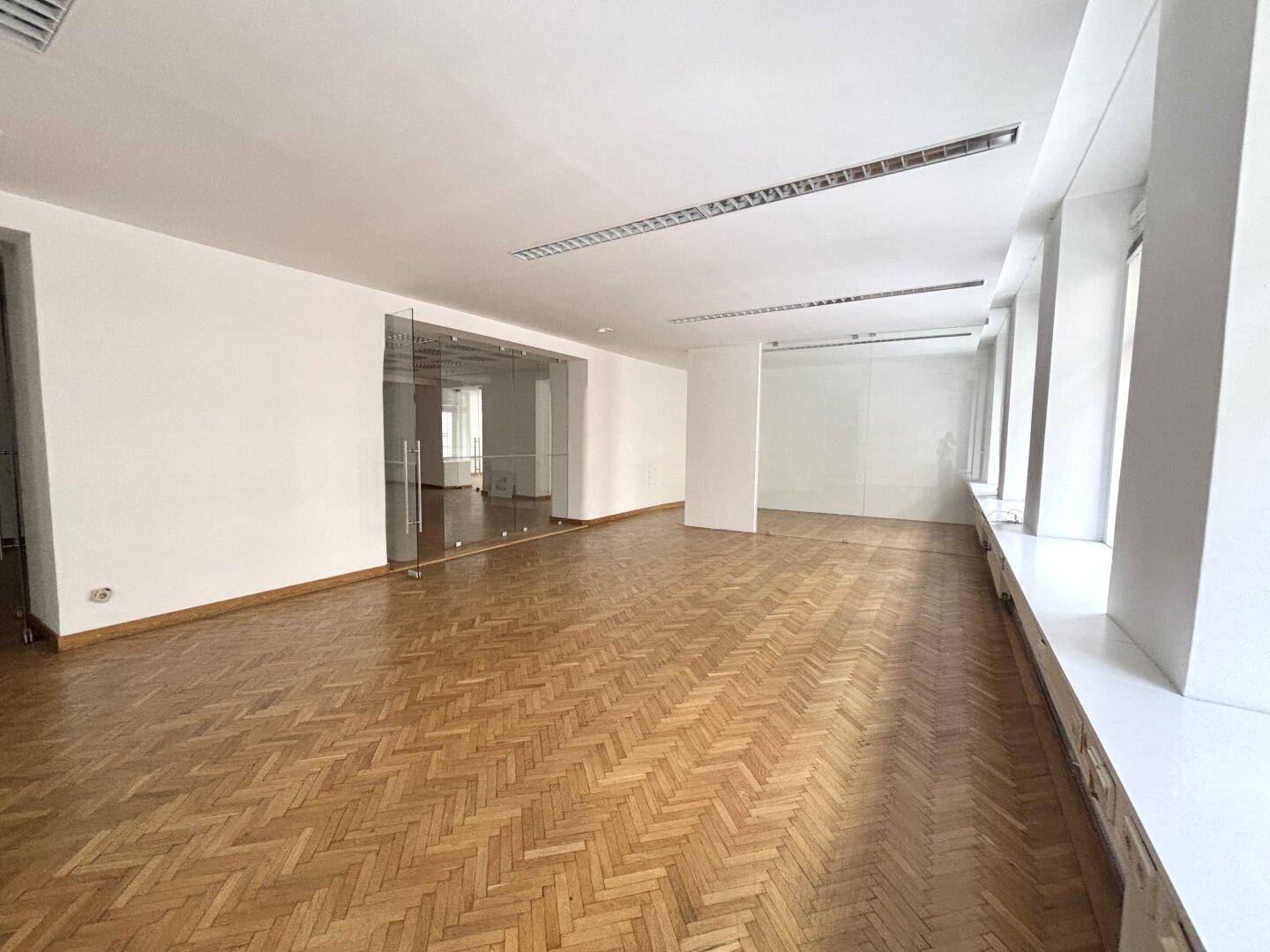 Weitläufiger Bürobereich mit elegantem Fischgrätparkett und durchgehenden Glaswänden für offene Gestaltung.