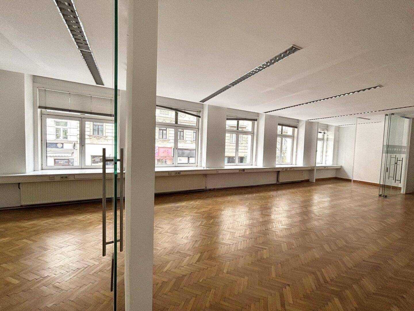 Heller Büroraum mit Blick auf die Straße, Fischgrätparkett und einer modernen Glasabtrennung.
