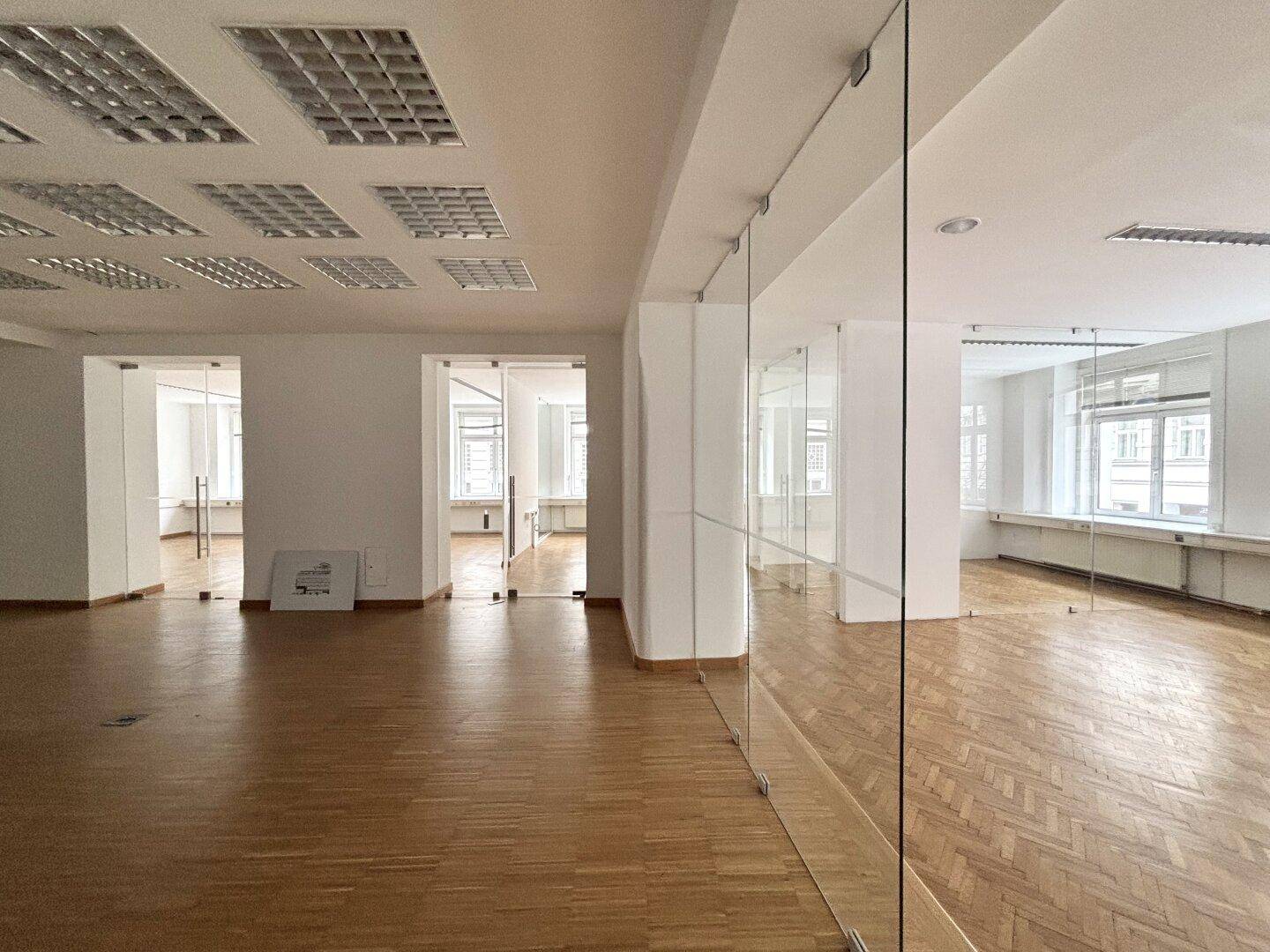 Heller Büroraum mit Glaswänden und Deckenleuchten, die eine moderne Arbeitsumgebung schaffen.