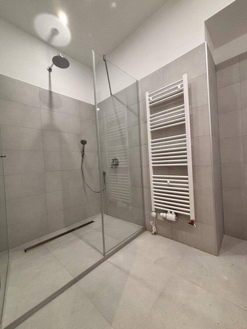 Moderne begehbare Dusche mit Regenduschkopf und Handtuchheizkörper im Badezimmer.