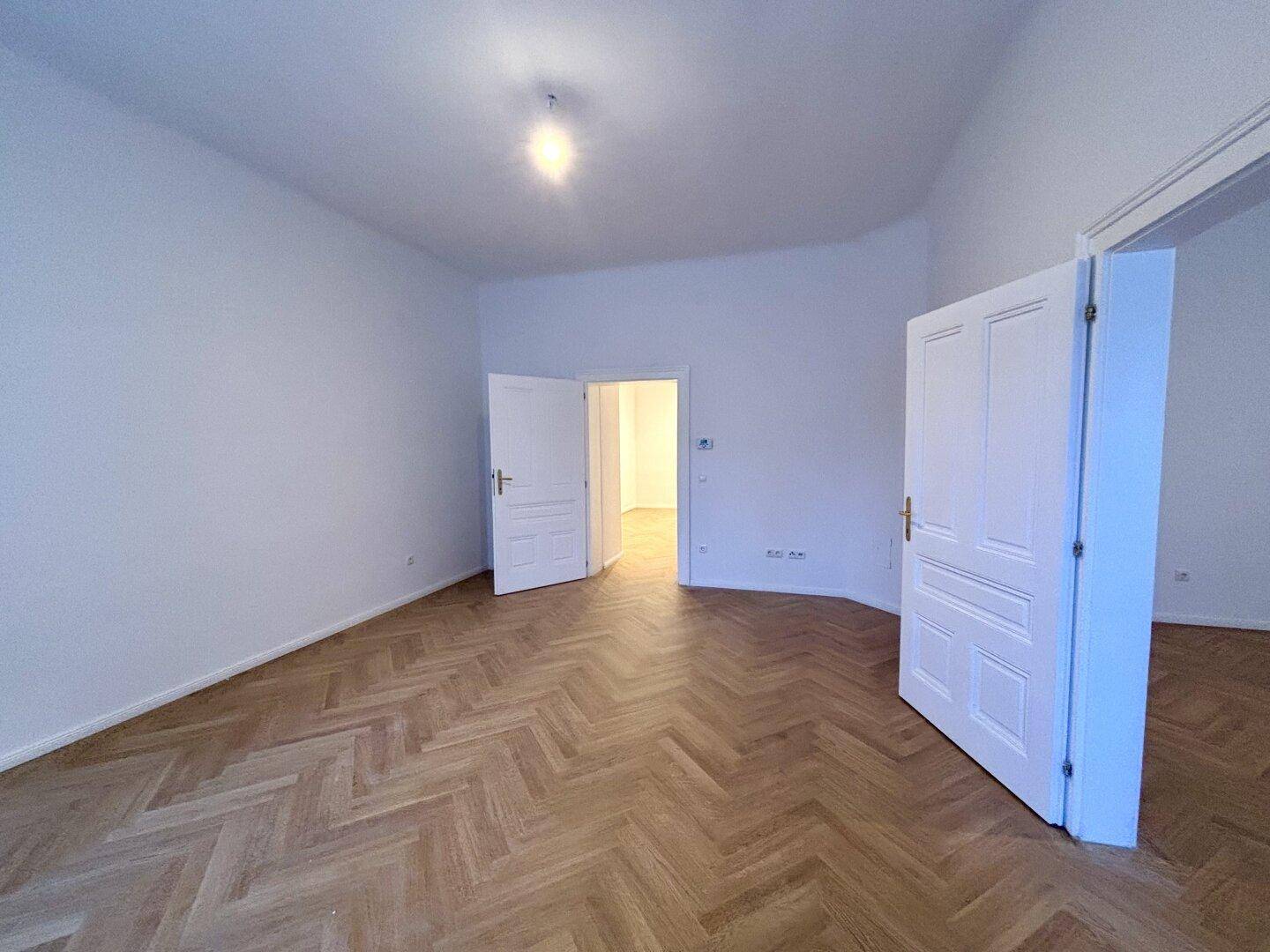 Geräumiger, heller Raum mit Fischgrätparkett und weißen Türen.