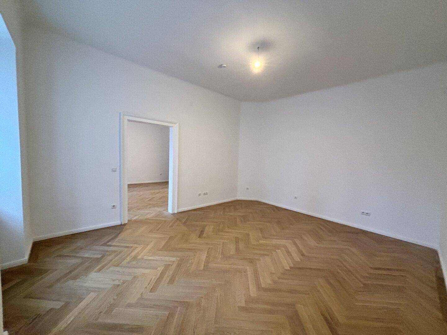Heller Raum mit Fischgrätparkett und Blick in einen weiteren Raum.