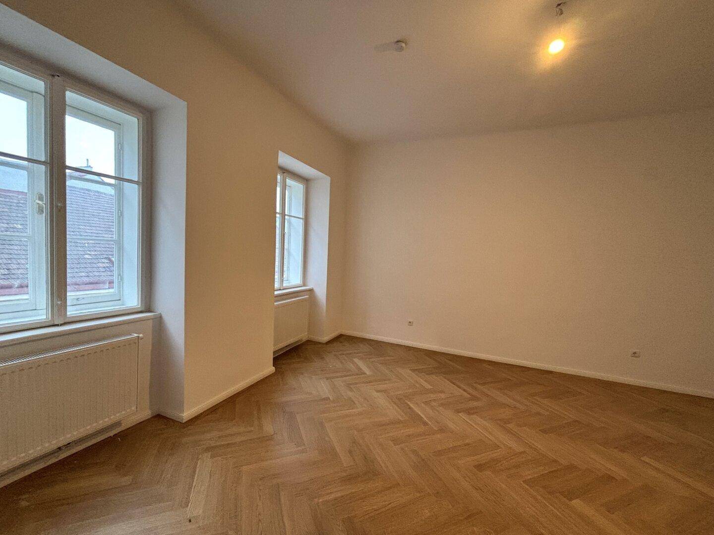 Heller Raum mit Fischgrätparkett und zwei Fenstern.