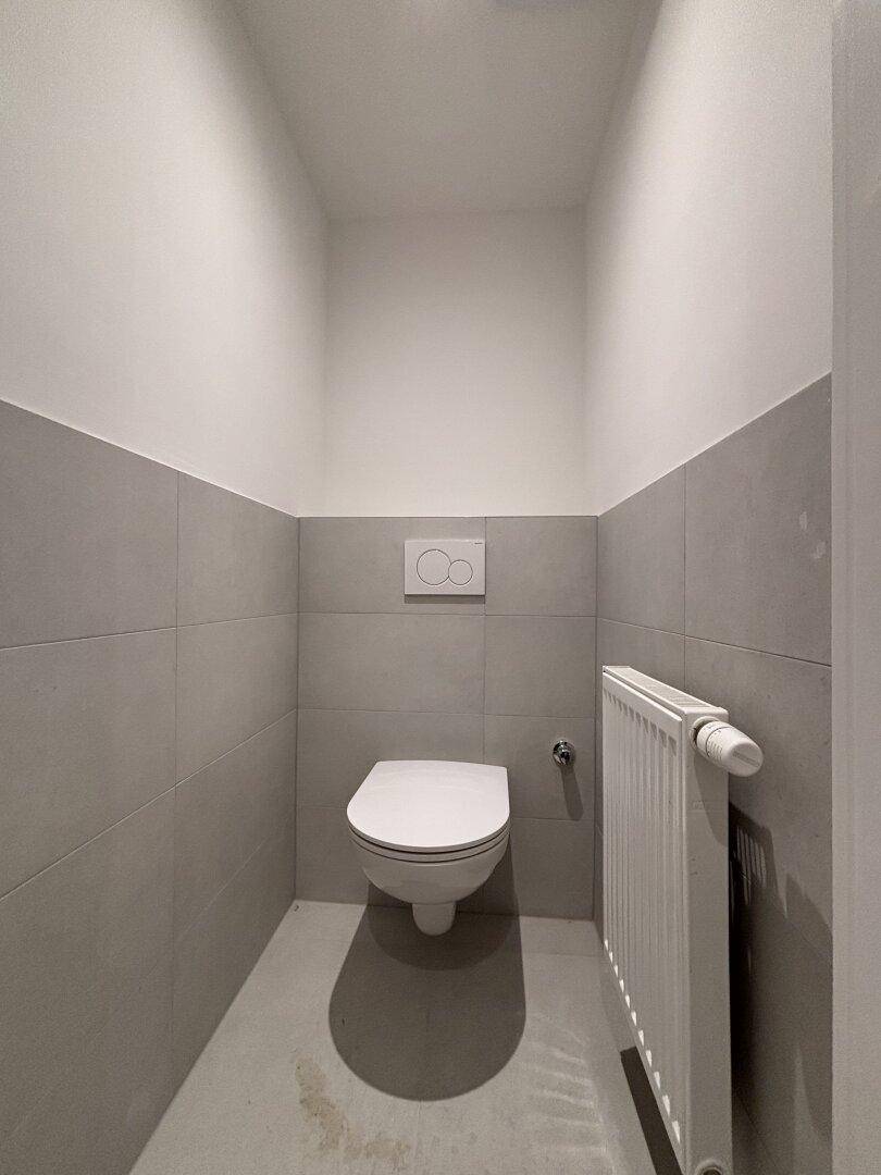 Modernes Gäste-WC mit Wand-WC, grauen Fliesen und Heizkörper.