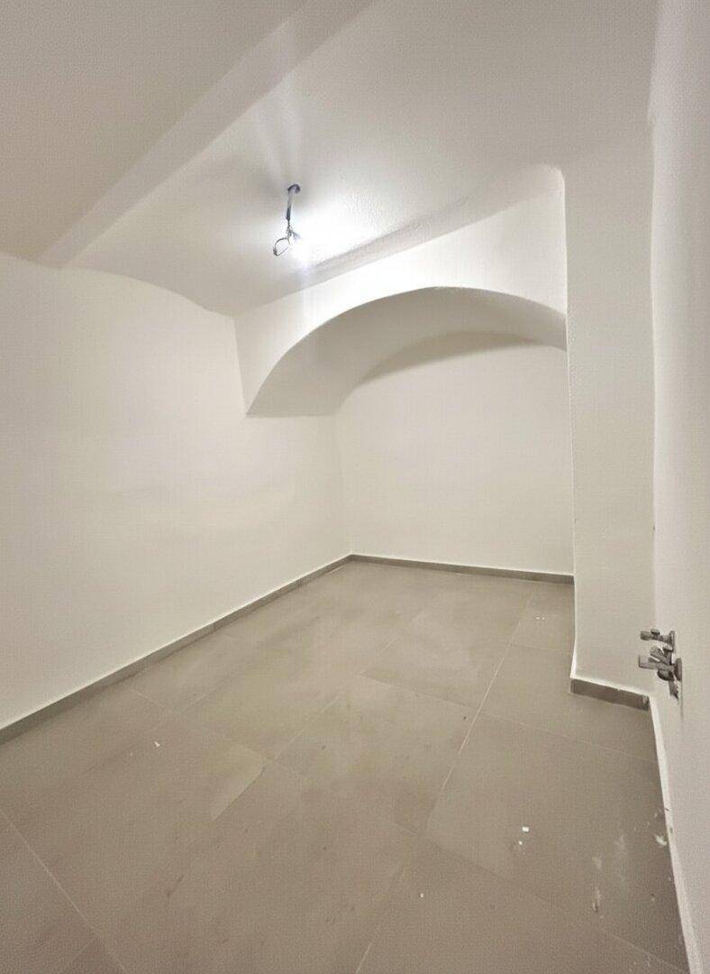 Kleiner, leerer Raum mit grauen Fliesen und einer gewölbten Nische an der Wand.