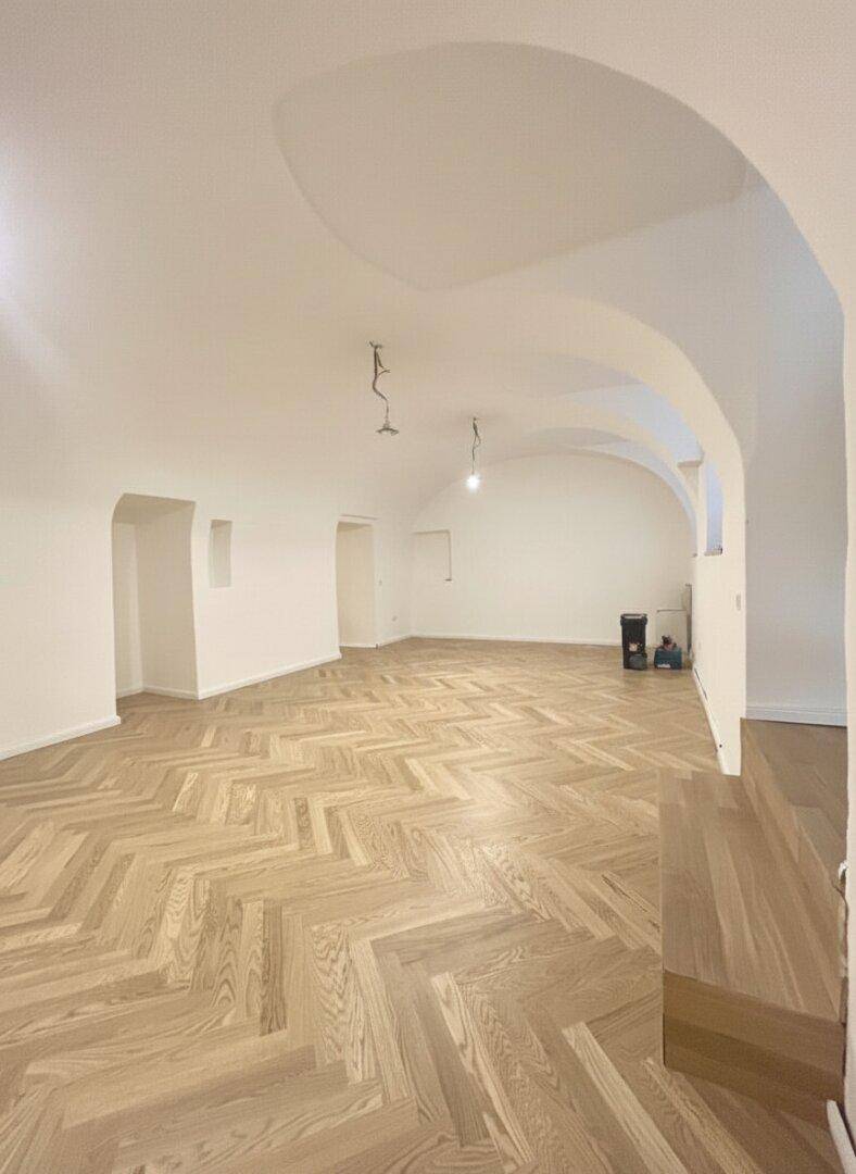 Großzügiger, heller Raum mit beeindruckenden Gewölbedecken und elegantem Fischgrätparkettboden.