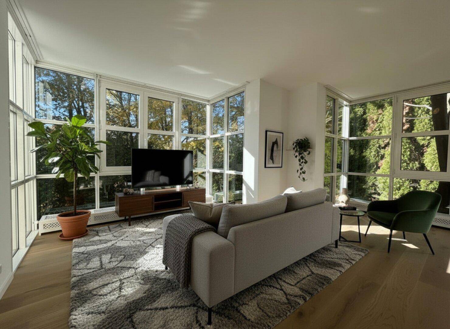 Helles Wohnzimmer mit großen Fenstern, Holzboden und moderner Einrichtung.