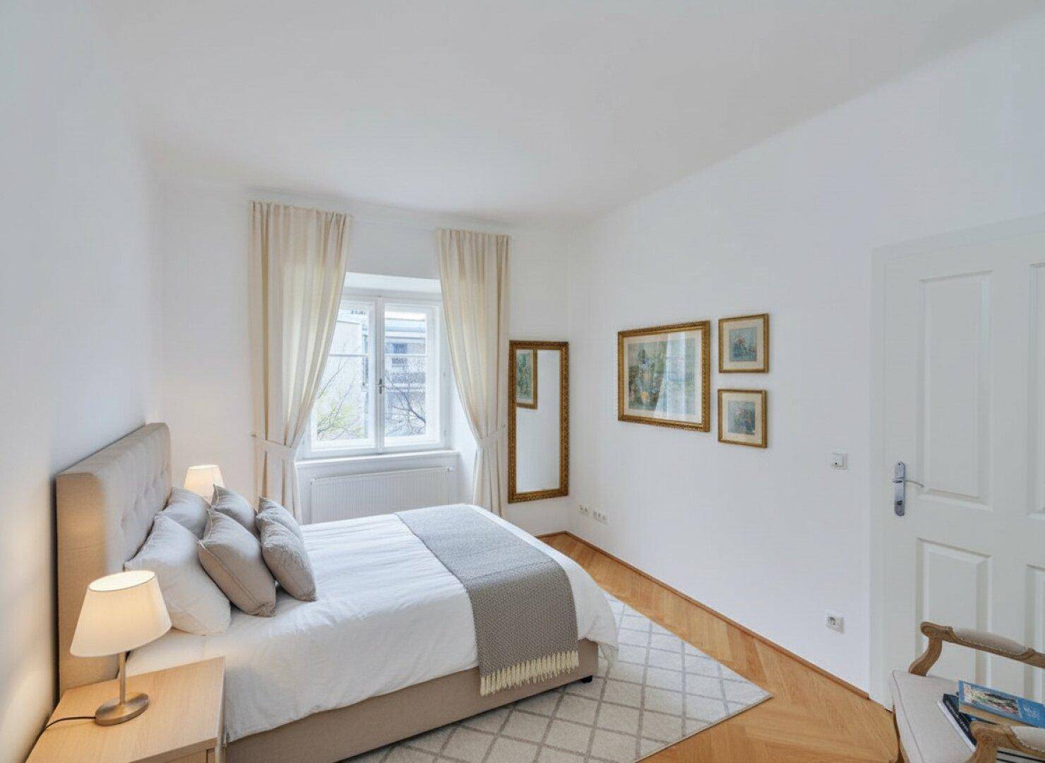 Gemütliches Schlafzimmer mit Doppelbett, Parkettboden und großem Fenster.