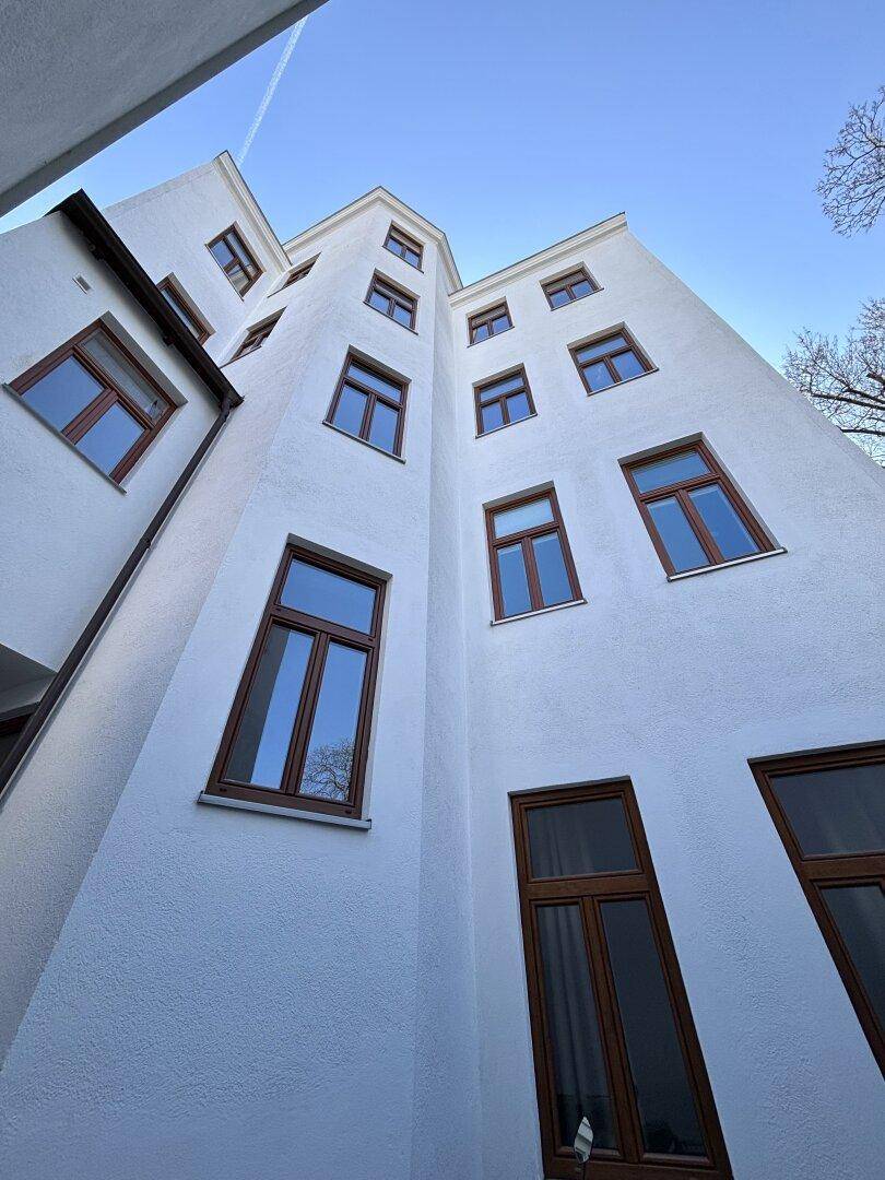 Innenhofansicht eines hohen Altbaus mit vielen Fenstern und weißer Fassade unter blauem Himmel.