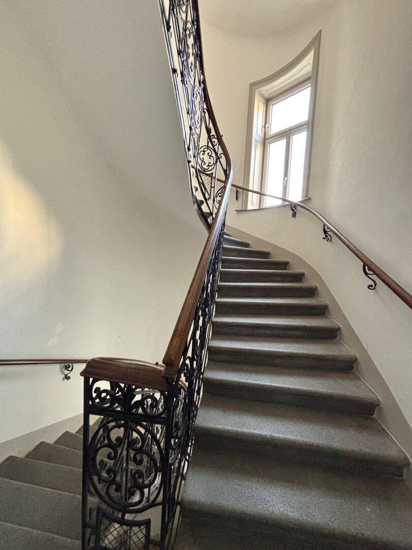 Geschwungenes Treppenhaus eines Altbaus mit schmiedeeisernem Geländer und natürlichem Lichteinfall.
