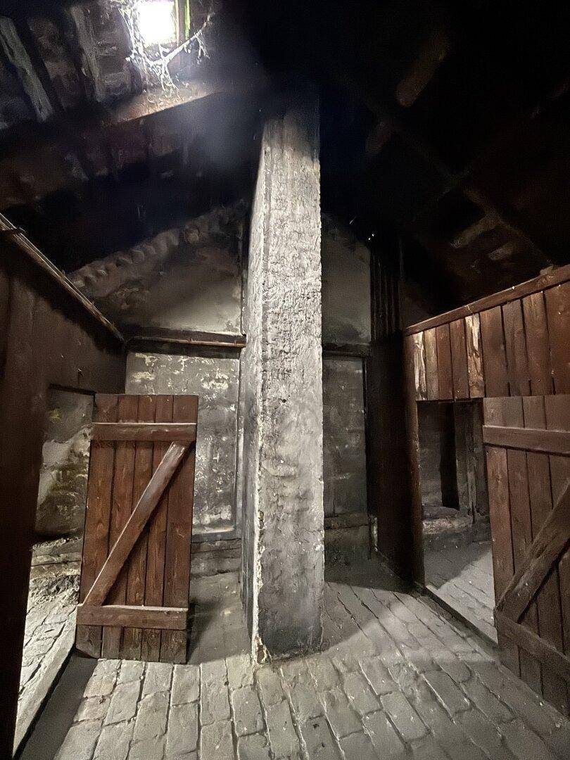 Rustikaler Dachboden mit Holztüren, Ziegelboden und sichtbaren Holzbalken unter dem Dach.