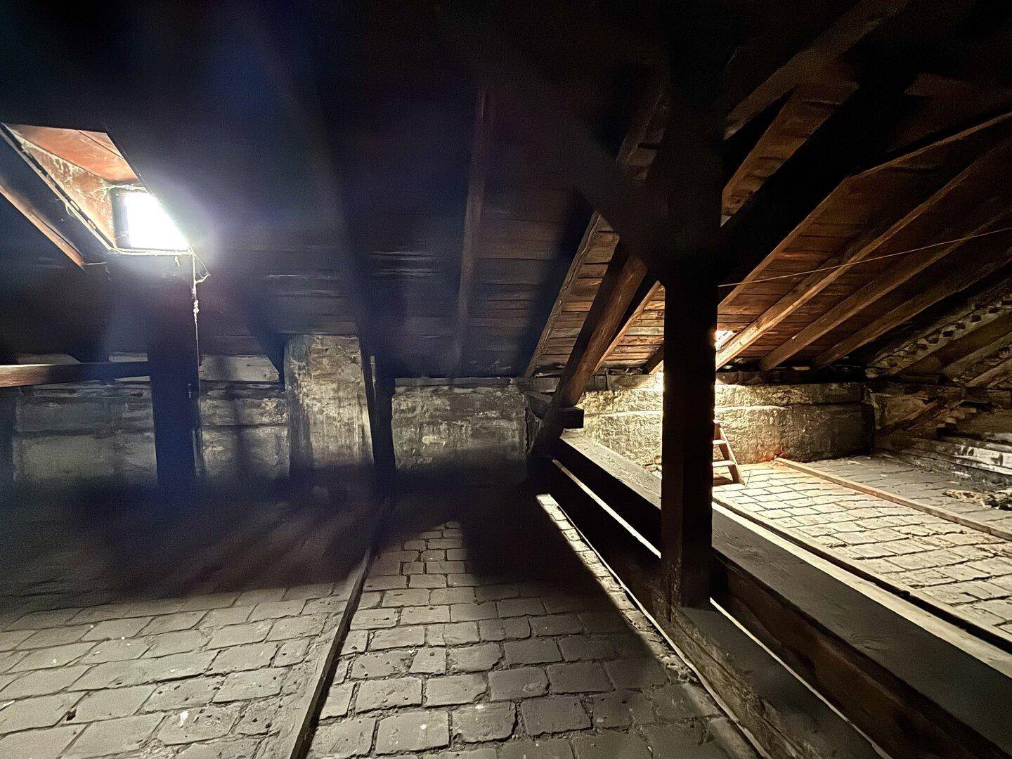 Geräumiger Dachboden mit Holzbalken, Ziegelboden und einem Dachfenster für natürliches Licht.