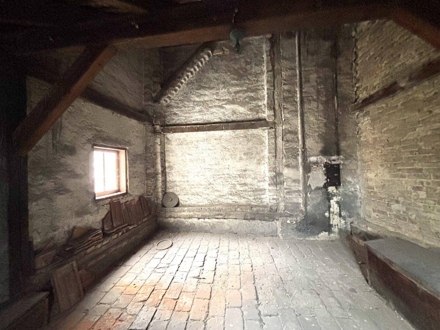 Großer Dachboden mit Ziegelboden, sichtbaren Holzbalken und einem Fenster für natürliches Licht.