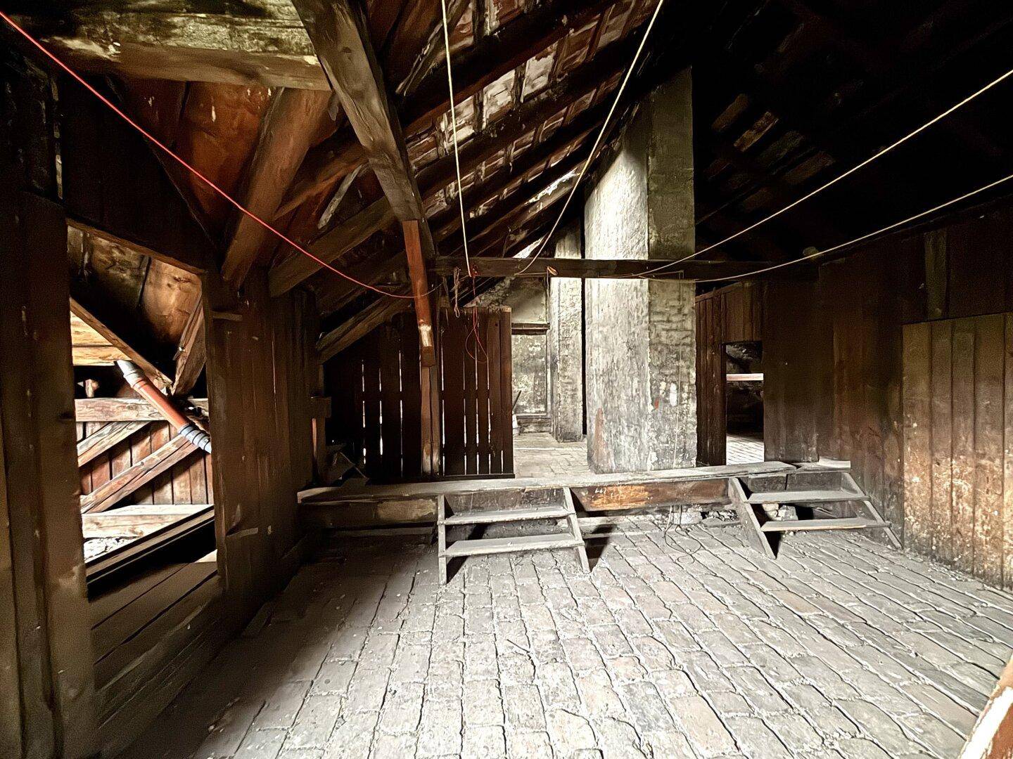 Großer Dachboden mit Holzbalken, Ziegelboden und Holzverkleidungen, bereit für den Ausbau.