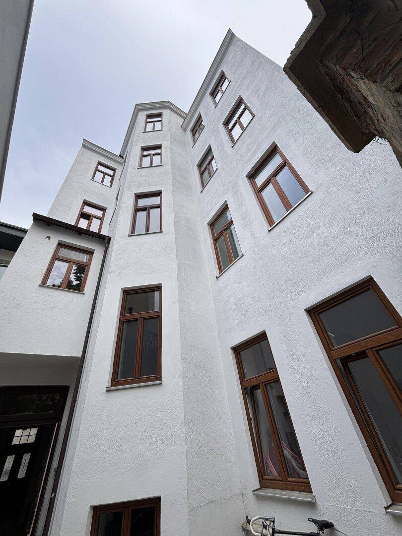 Innenhofansicht eines hohen Altbaus mit vielen Fenstern und weißer Fassade unter bewölktem Himmel.