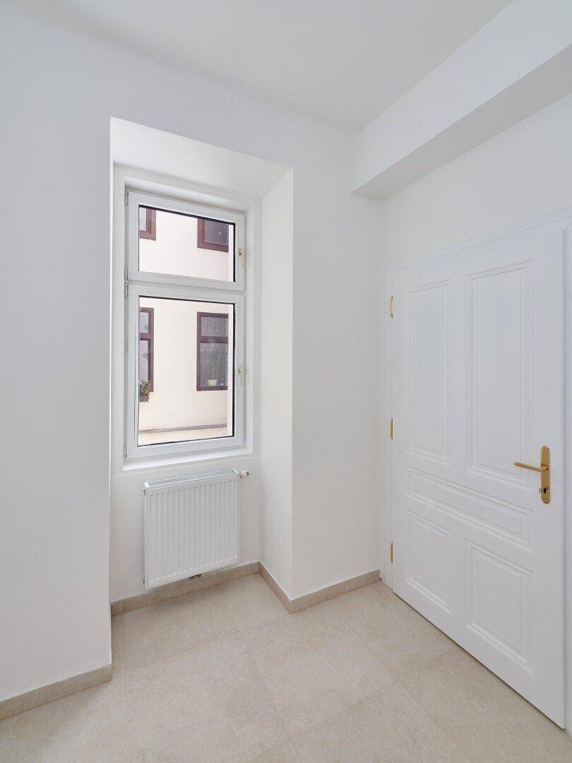 Kleiner Raum mit Fliesenboden, einem Fenster und weiß gestrichenen Wänden, bereit für die Nutzung.