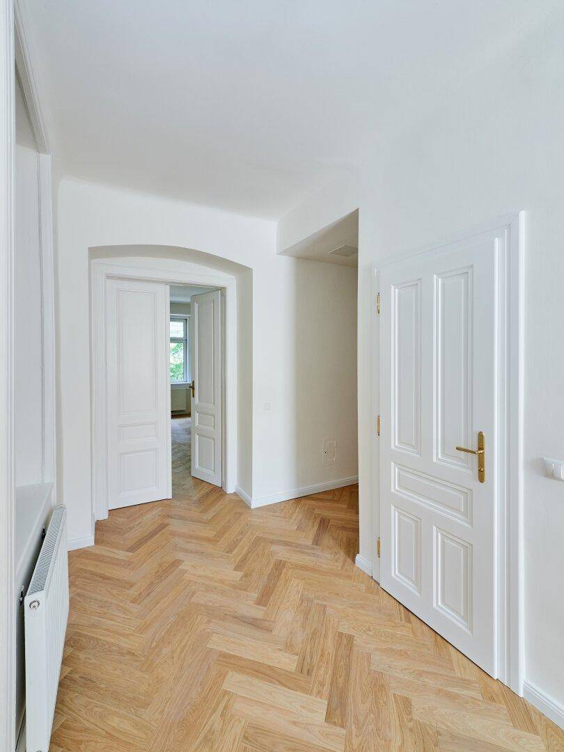 Flur mit Fischgrätparkett und eleganten weißen Türen, die zu weiteren Räumen der Wohnung führen.