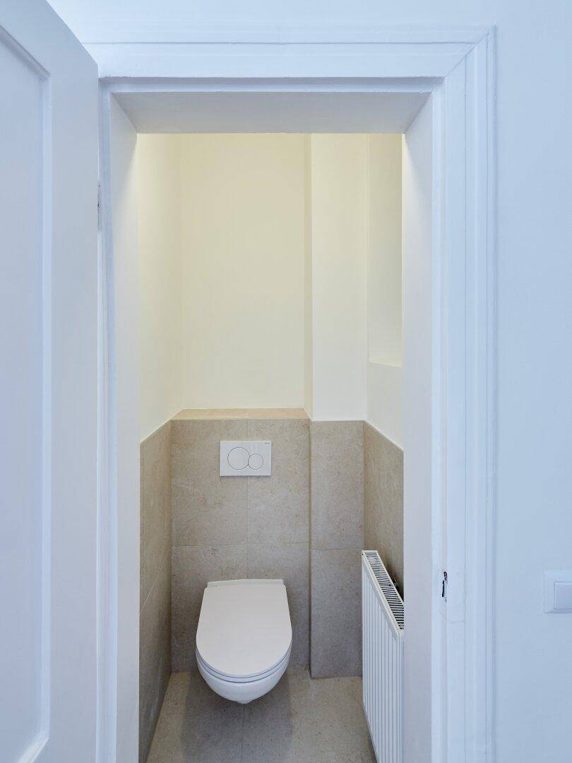 Modernes Gäste-WC mit Wand-WC, halbhohen Fliesen und einem Heizkörper, schlicht und funktional.